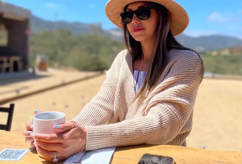 Lucero Galiano con sombrero, sentada al aire libre con una taza de café
